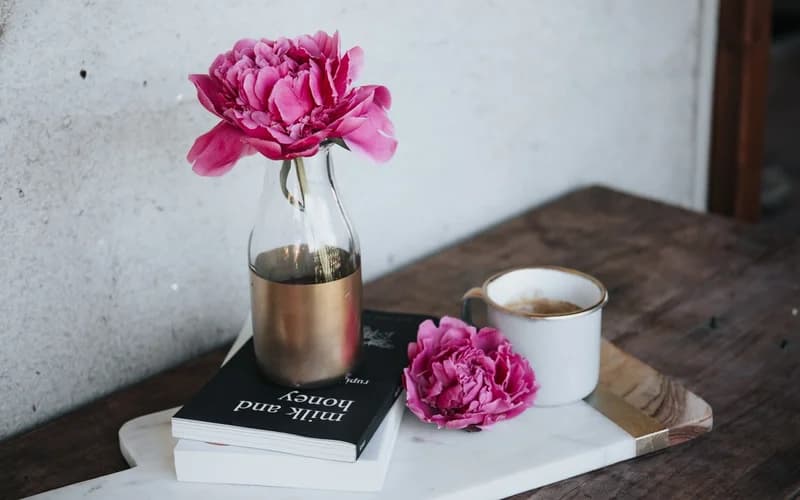 På bildet: en vase med blomst, bøker og kaffekopp på et bord