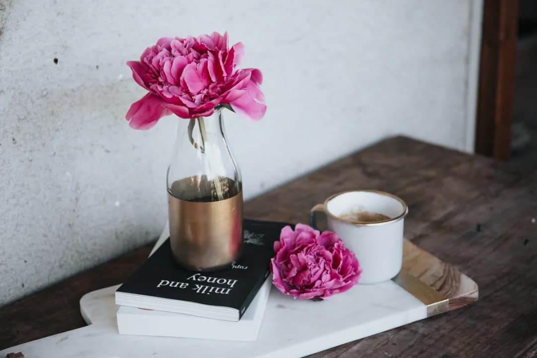 På bildet: en vase med blomst, bøker og kaffekopp på et bord