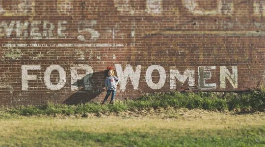 Ei jente står foran en murvegg der det står skrevet "For women" 