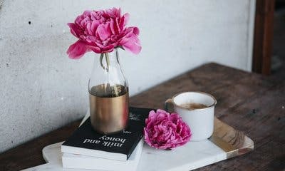 På bildet: en vase med blomst, bøker og kaffekopp på et bord