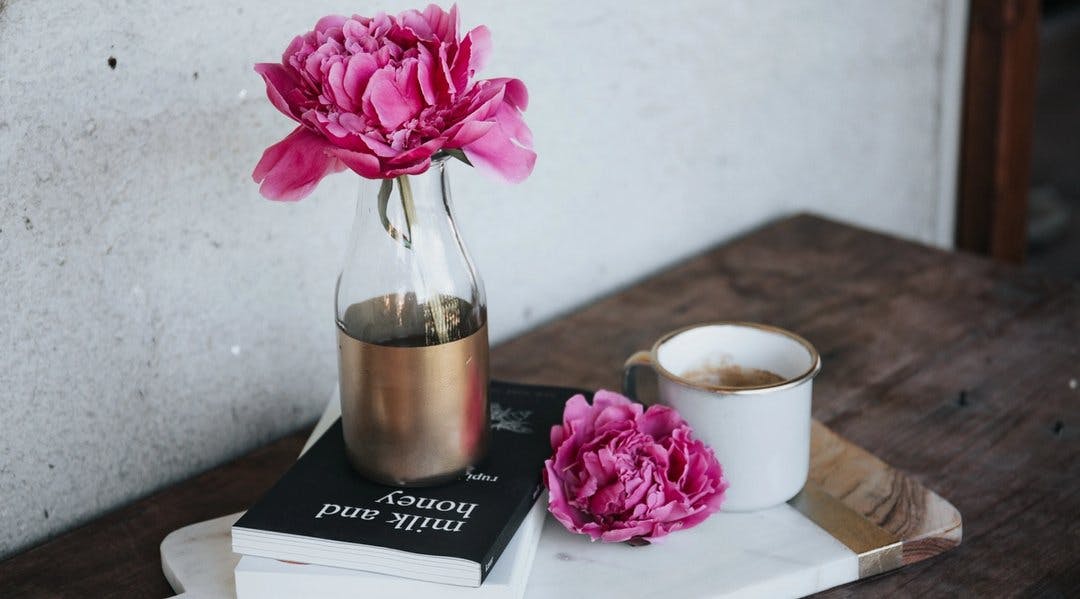 På bildet: en vase med blomst, bøker og kaffekopp på et bord